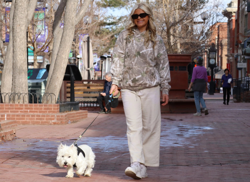 Woman walking a dog on a city street with trees and buildings in the background