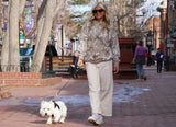 Woman walking a dog on a city street with trees and buildings in the background